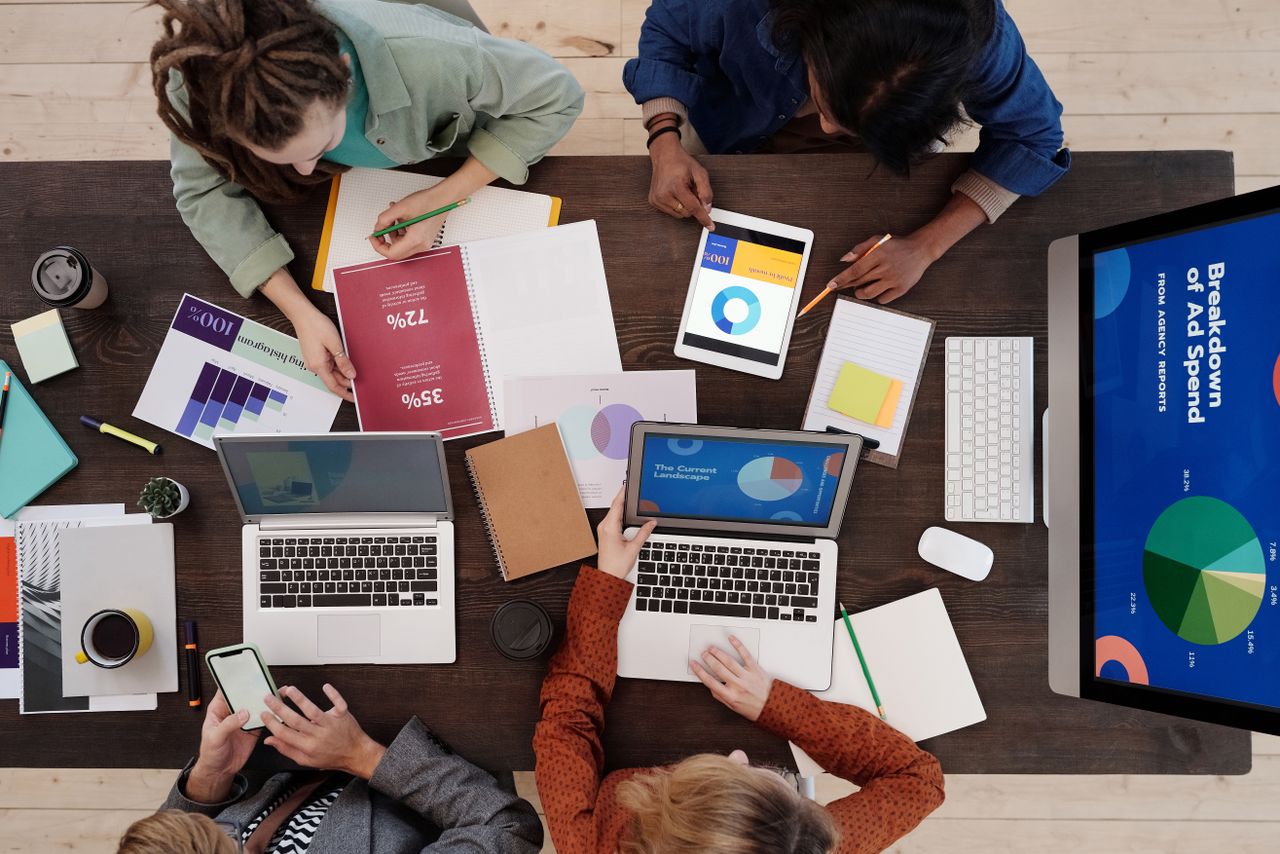 Raznoliki tim koji sarađuje na strategijama digitalnog marketinga za stolom, koristeći laptope i tablete.